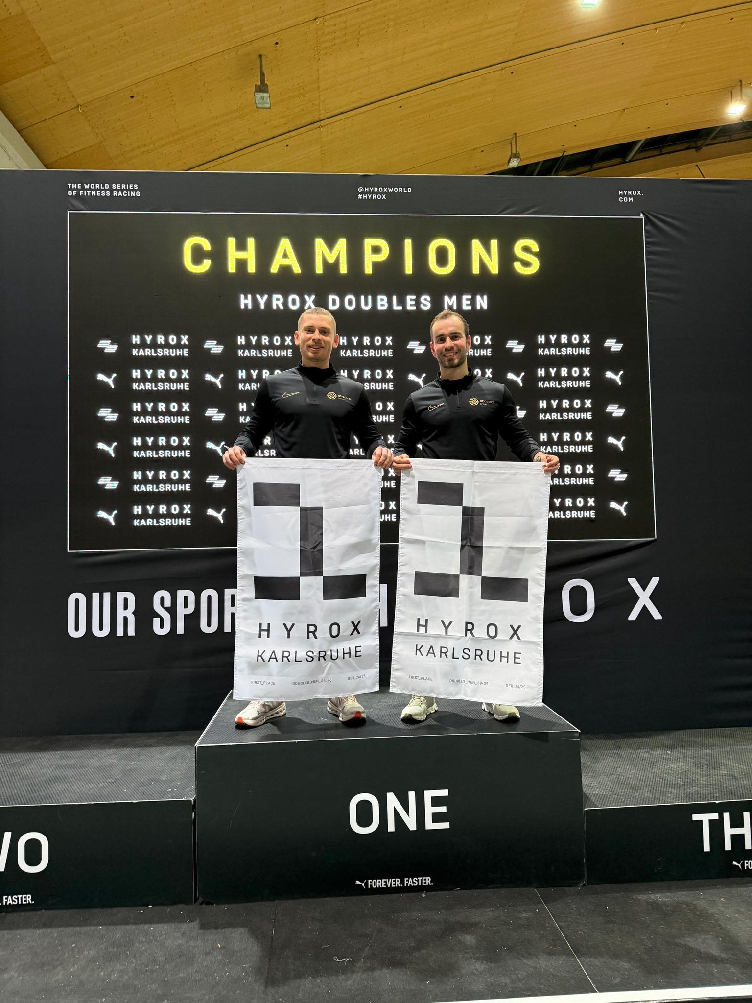 Hyrox Siegehrung in Karlsruhe: Zwei Männer auf Siegertreppe